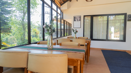 Bright resort dining space featuring large glass windows, green views, wooden tables, and neutral seating.