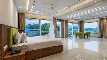 a king size bed beside the floor to ceiling windows in the suite at Corbett Four Seasons, Ramnagar