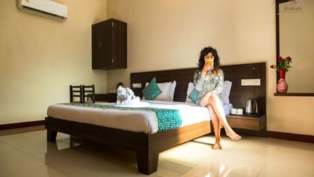 A woman sitting on a bed in a guest room featuring wooden furnishings and an air-conditioning at Daksh Resort & Amusement Park.