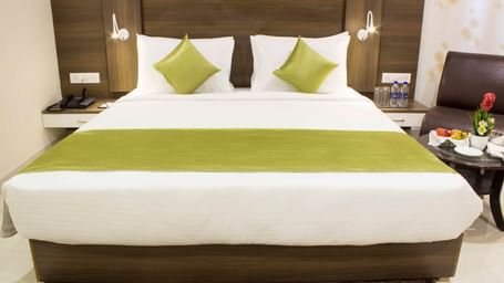 A hotel room with a clean bed, white sheets, and a decorative headboard | Daksh Comfort Room | Daksh The Madhuvan Suites