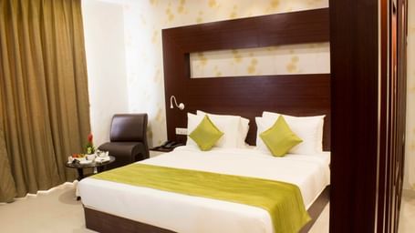 A hotel bedroom with a large bed, elegant wooden headboard, and green bed runner | Daksh Suite | Daksh The Madhuvan Suites