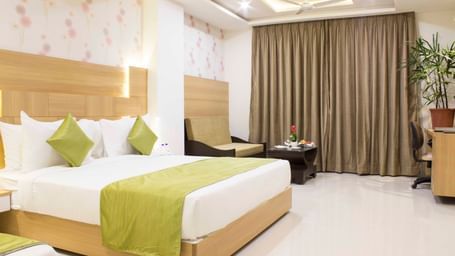 A hotel bedroom with a large bed, a single bed, light wood headboards, and green bed runners | Daksh Pride Room | Daksh The Madhuvan Suites