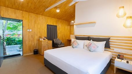 image featuring a double bed with the entrance door open with lush green views at the premium room - Darza Resorts