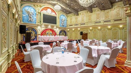 Ornate banquet hall at Diamond Palace Lords Plaza with round tables, chairs, chandeliers, and decorative walls.