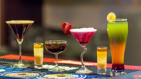 Assortment of colorful cocktails and shot glasses arranged on a bar counter with a blurred background.