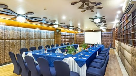 Meeting room with a U-shaped table covered in fabric, facing a projection screen and decorated walls.
