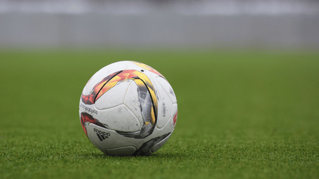 A colourful football rests on the lush grass of a modern sports pitch.