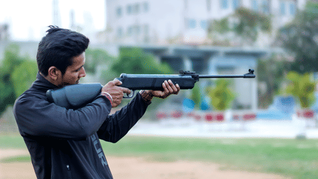 A man takes careful aim with a rifle at an outdoor shooting range - District Gravity Adventure Park, Hyderabad