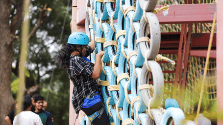 A person wearing a blue safety helmet climbs up a challenging tyre wall - District Gravity Adventure Park, Hyderabad