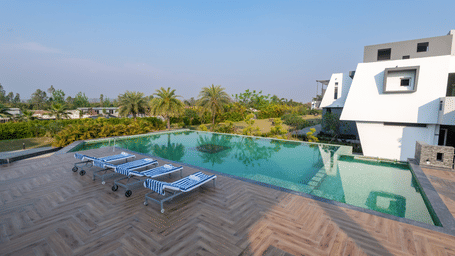 Pool area with lounge chairs placed beside it, offering a view of trees on one side at DLS Forest Vines Resort.