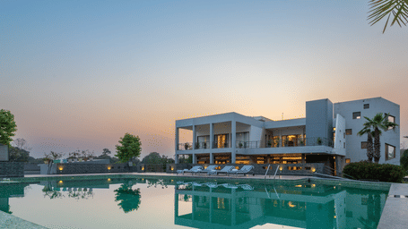 Facade view of DLS Forest Vines Resort with its reflection shimmering on the swimming pool under a clear sky.