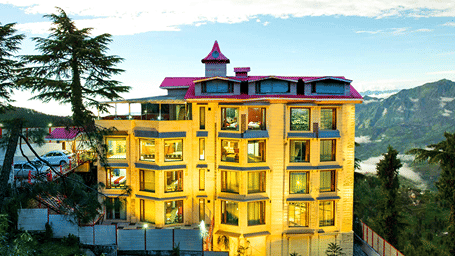 Facade of the DLS Rock Castle, Shimla featuring a well lit multiple storey building surrounded by trees and plants.