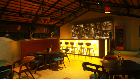 A bar area at DNC Shevaroys Resort & Spa featuring a back-lit counter, tall stools, and a dark pitched roof.