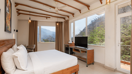 Bedroom with bed facing large windows and outdoor greenery view at Ekawa Ganga, Rishikesh.