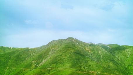 An overview of a rolling hill that is covered in greenery with blue sky in the background.
