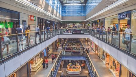 An overview of a mall with glass roof and a view of two floors with people walking.