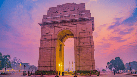 Evening view of India Gate with glowing arch and dramatic pink-purple sky.