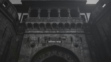 A dramatic, low-angle shot of the historic, stone-carved entrance gate at Shaniwar Wada fort in Pune.