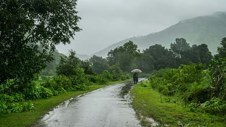 An overview of a road with monsoon rains and a person holding an umbrella and walking.