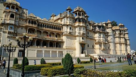 Facade view of City Palace in Udaipur with a garden and people in front of it.
