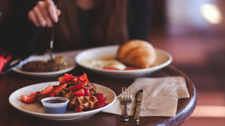 Waffle with strawberries and a croissant served on a round coffee table in a cafe. 