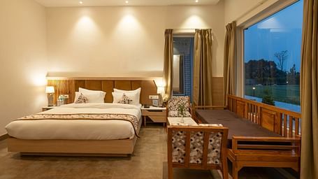 A cosy hotel room with a king-size bed, a seating area, and a view of the lush green outdoors.