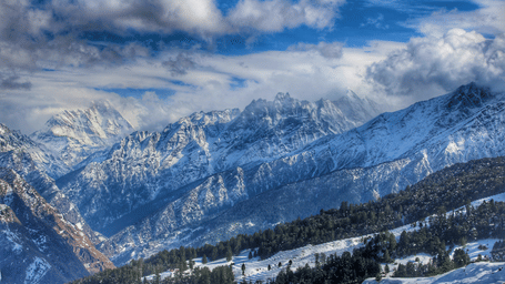 High-altitude view of snow-clad mountains under cloudy skies at Mini Switzerland in Uttarakhand.