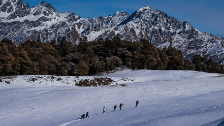 Snow-covered ski slope beneath rugged Himalayan peaks, with scattered visitors enjoying the winter landscape under clear blue skies