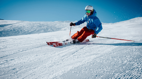 A skier racing down a pristine slope under a clear blue sky, enjoying winter adventure in Auli, the Mini Switzerland of India.