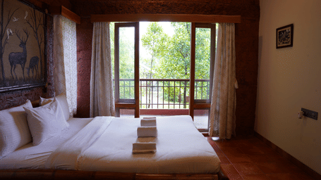 Bedroom with double bed balcony door and view of outdoor greenery at Forest Escapes.
