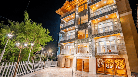 The multi-storey exterior of the hotel illuminated at night with warm golden lights - Golden Oak By The Lake Hill, Khurpatal