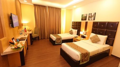 Hotel room with a bed featuring striped bedding and a television on the wall - Grand Plaza Lords Inn Jammu