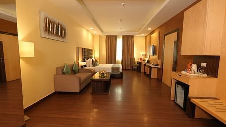 Hotel suite hallway leading to a seating area and a bed with striped bedding - Grand Plaza Lords Inn Jammu