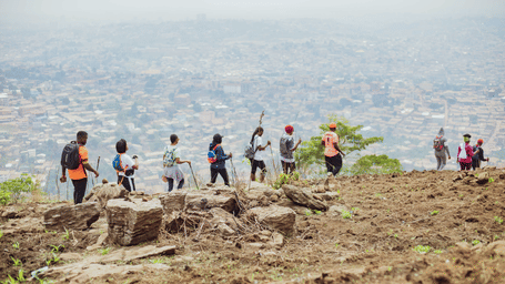 Hikers walking along a rocky hilltop trail with panoramic views of the city below from the summit.