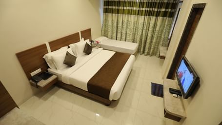 Extended view of the queen size bed and single bed facing the wall-mounted TV in the Deluxe Room of Highland Resort.