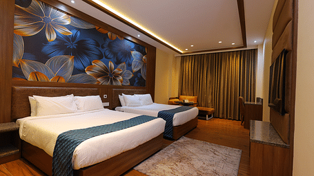 Side angle image of a Suite at Amar Hotel with two beds, table, TV and a painting