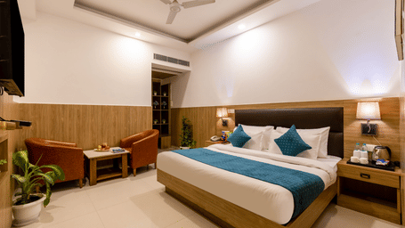 Deluxe Room at Hotel Corporate Suites featuring a double bed with lamps lit on both sides over the nightstands and seating space against the wall