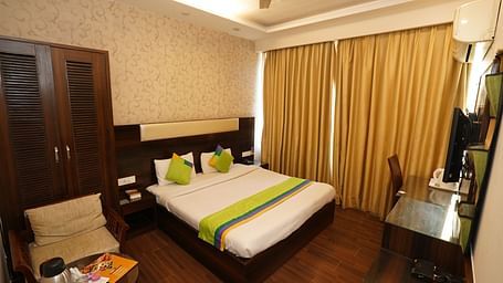 Deluxe Room featuring a king size bed with green accents, a wooden headboard, bedside tables, curtains, a desk, and a chair.- Hotel Dreamland, Chandigarh