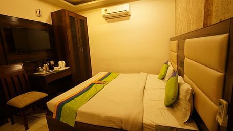 Standard Room furnished with a bed featuring white linens and green and yellow accents, two pillows, a chair, a desk, a television, and a wardrobe. - Hotel Dreamland, Chandigarh