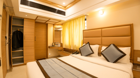 Queen bed with white linens, accent pillows, padded headboard, air conditioning vents, and wardrobe in a guest room at Hotel Grand Sabarees Madurai.