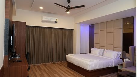 full view image of the suite with a comfortable double bed and a wall mounted television right opposite to it with closed curtains - Hotel Grand Sigma
