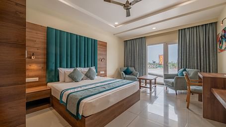 Elegant room with king size bed, full-length curtains, and work station with a seating area nearby at Hotel Highway King, Bilaspur.