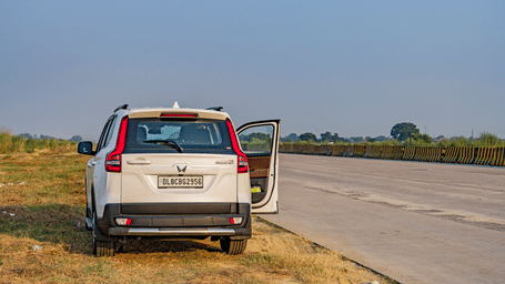 A white car resting on the side of a highway with one of its door open.
