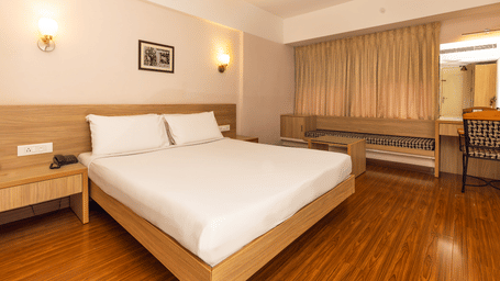 A minimalist room with a queen size bed, light wood furniture, a wall art, and a bedside table at Hotel Horizon, Trivandrum.