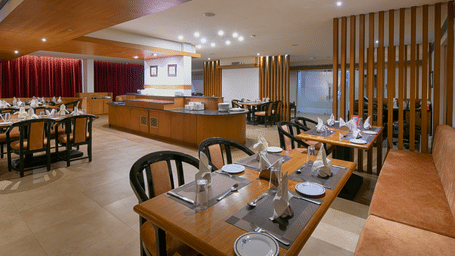 A restauratn featuring wooden tables and chairs, a buffet counter in the background, and wooden slat room dividers at Hotel Horizon, Trivandrum.