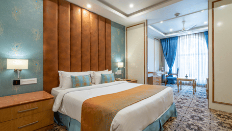 Wide shot of a contemporary hotel room with a spacious bed, nightstands, and a teal and terracotta colour scheme at Hotel Hukam's Lalit Mahal.