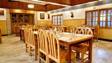 A wide shot of the main dining hall at Hotel Mamallaa Heritage, filled with numerous wooden tables and chairs, ready for guests.