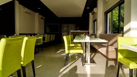 A spacious and brightly lit interior of the restaurant at Hotel Mamallaa Heritage, with tables and chairs arranged for dining, receiving ample natural light.
