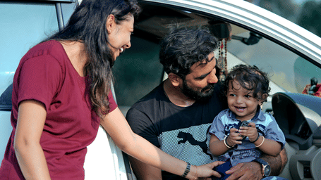 A man and a woman smiling at a young child sitting inside a car next to an open door.