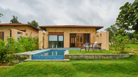 A wide exterior view featuring a tan building with a private swimming pool surrounded by a green lawn at Hotel Sonar Bangla, Ajodhya Hills.